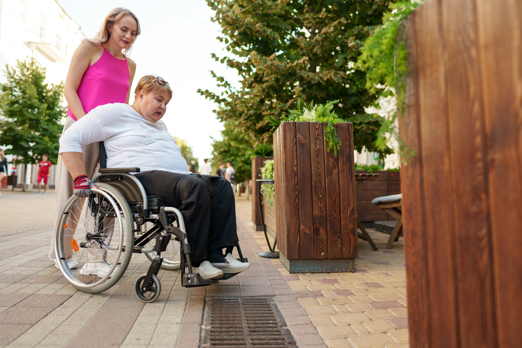 Young female caregiver pushing wheelchair with female person with disability across city street